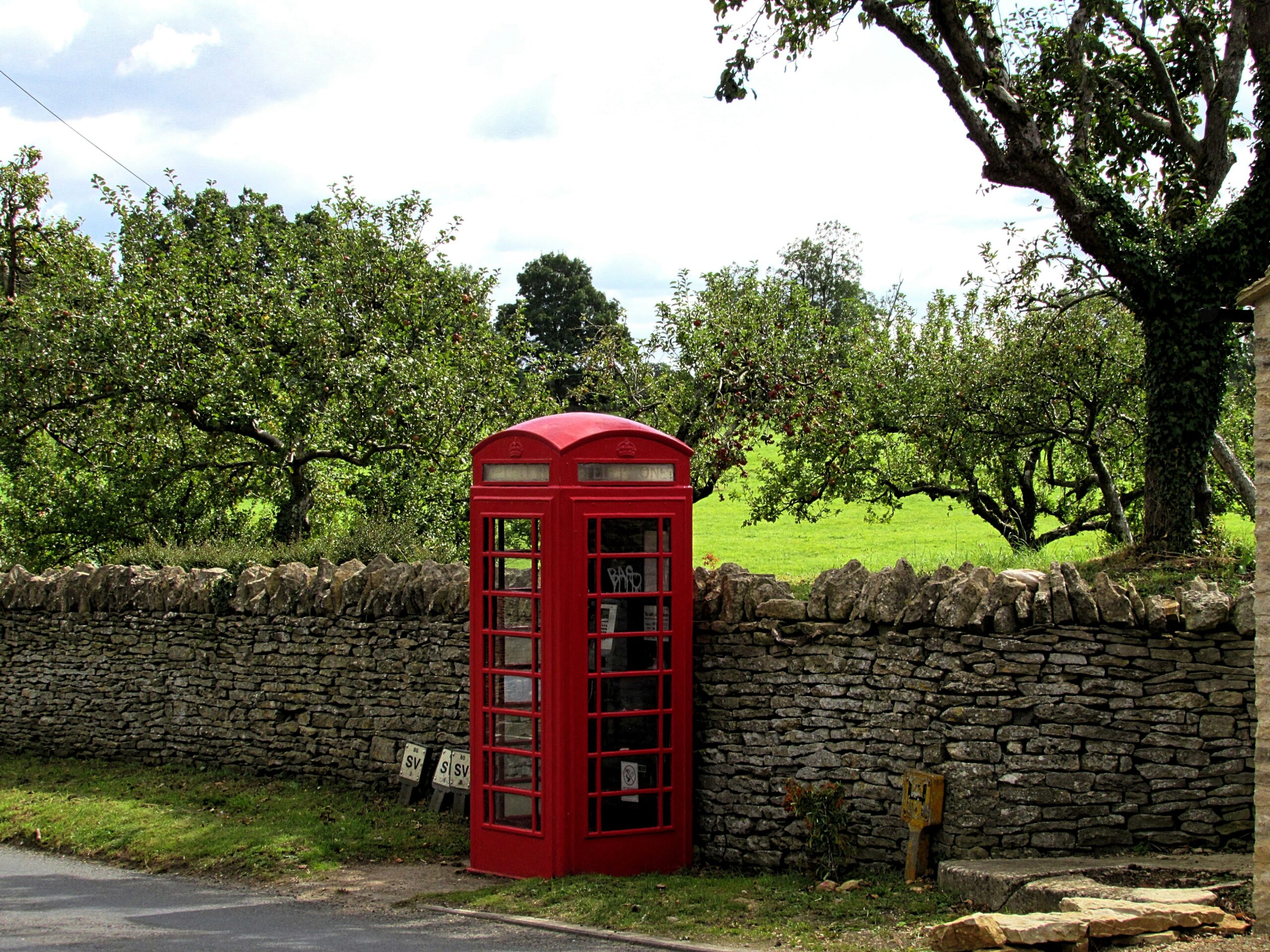 Classic red british phone box set against a cotswold stone wall and orchard near cirencester, capturing the charm of rural village life in the cotswolds.